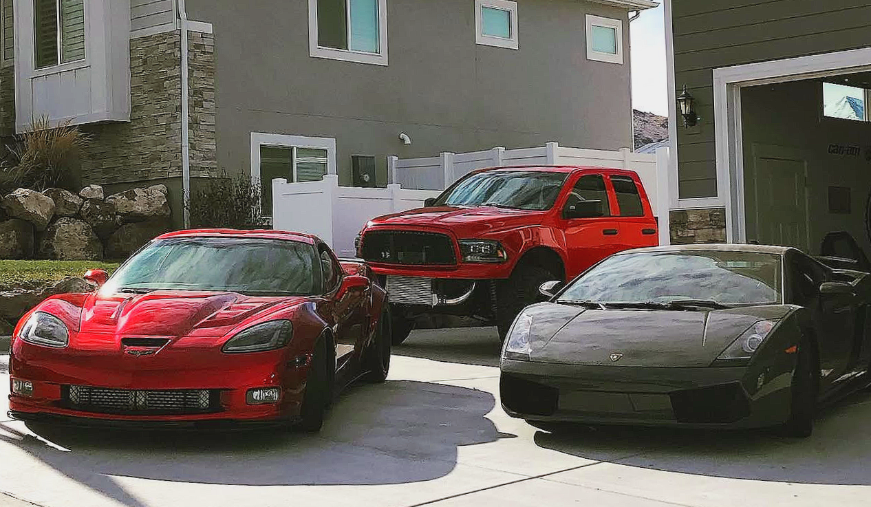 Three cars parked in a driveway for RG Motors. The cars are a red Corvette, a red Ram 1500, and a black Lamborghini.