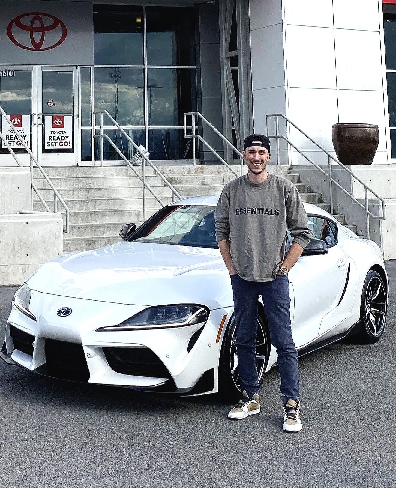 Ethan Ashby in casual clothing standing next to a white Toyota Supra car outside a Toyota dealership. Zotic Rentals, Onyx Rentals & RG Motors