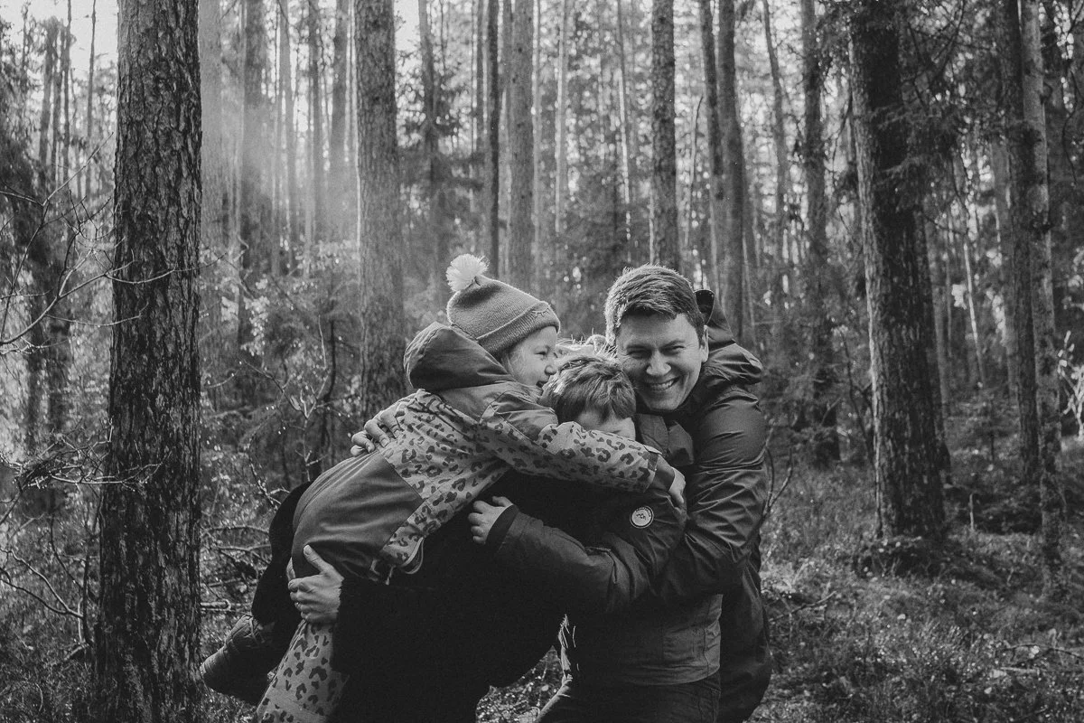 A family in a forest hugging each other, smiling, in black and white.