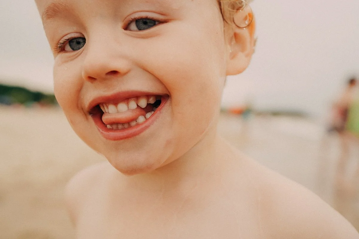 Close-up of a young boy smiling and sticking out his tongue at the beach.