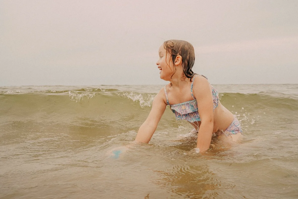 A young girl in a colorful swimsuit playing in the ocean waves, smiling and enjoying her time at the beach.