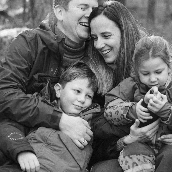 A happy family of four, including a man, woman, and two children, sitting outdoors and sharing a joyful moment.