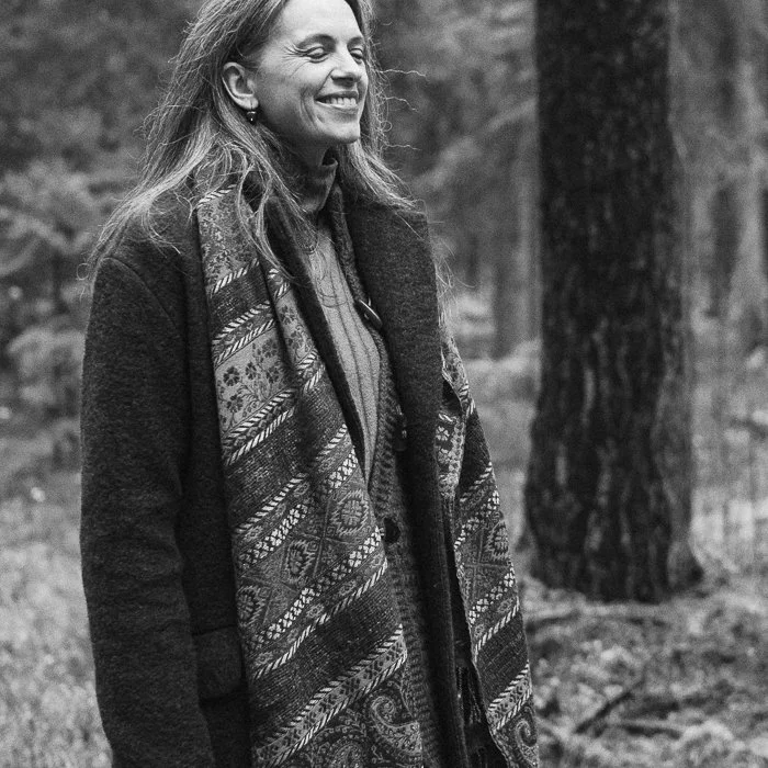 A smiling woman standing outdoors near trees in a forested area.