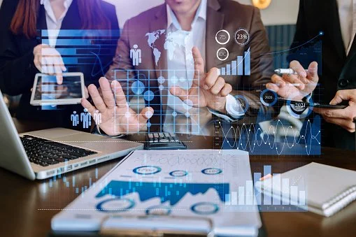 Reunión de negocios con personas usando dispositivos electrónicos y gráficos de datos flotando en la imagen.