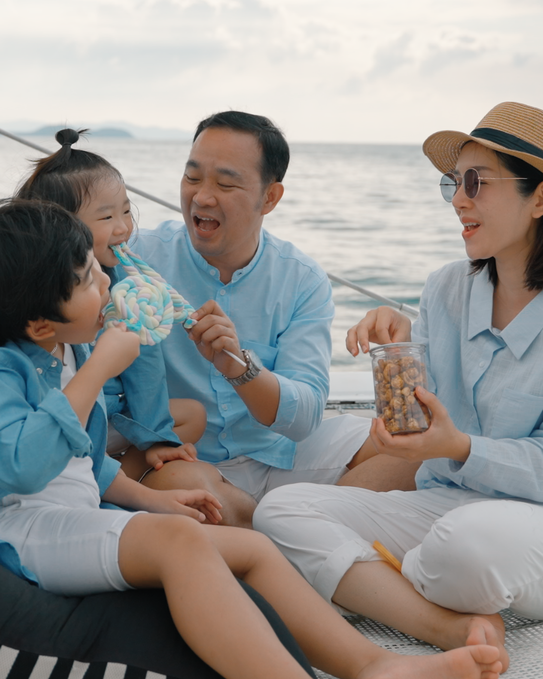 A family of four enjoying a day on a boat, with two children and parents smiling, sharing snacks, and playing together by the water, wearing casual summer clothes and sunglasses.