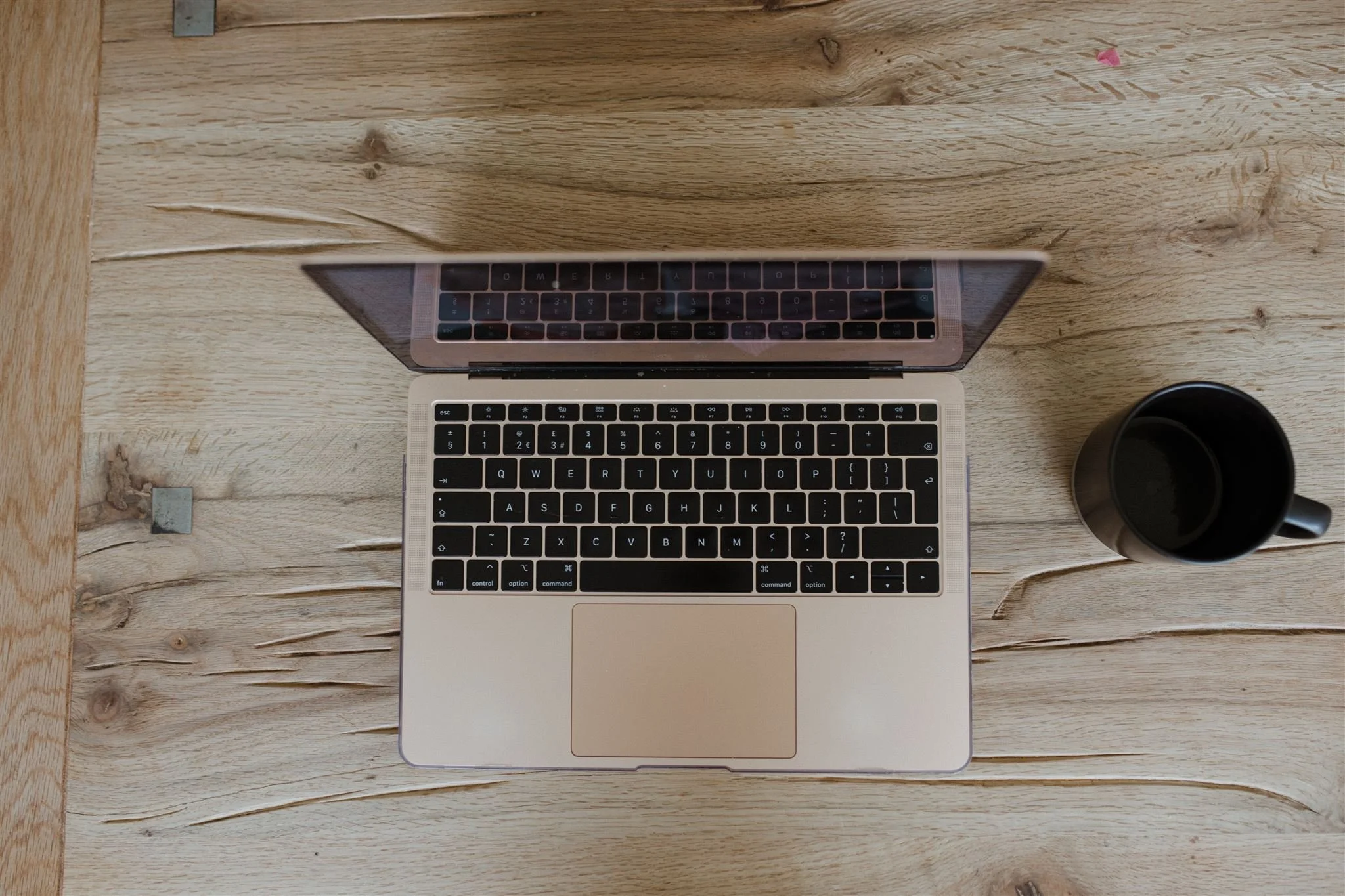 Top-down view of a laptop with black keyboard and a black mug on a wooden surface.