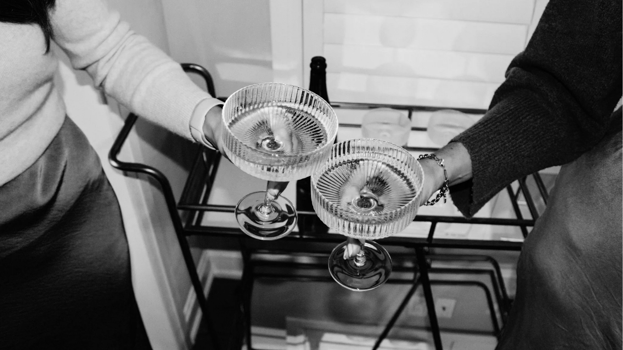 Two people clinking glasses of champagne at a celebration, seen from overhead in black and white.