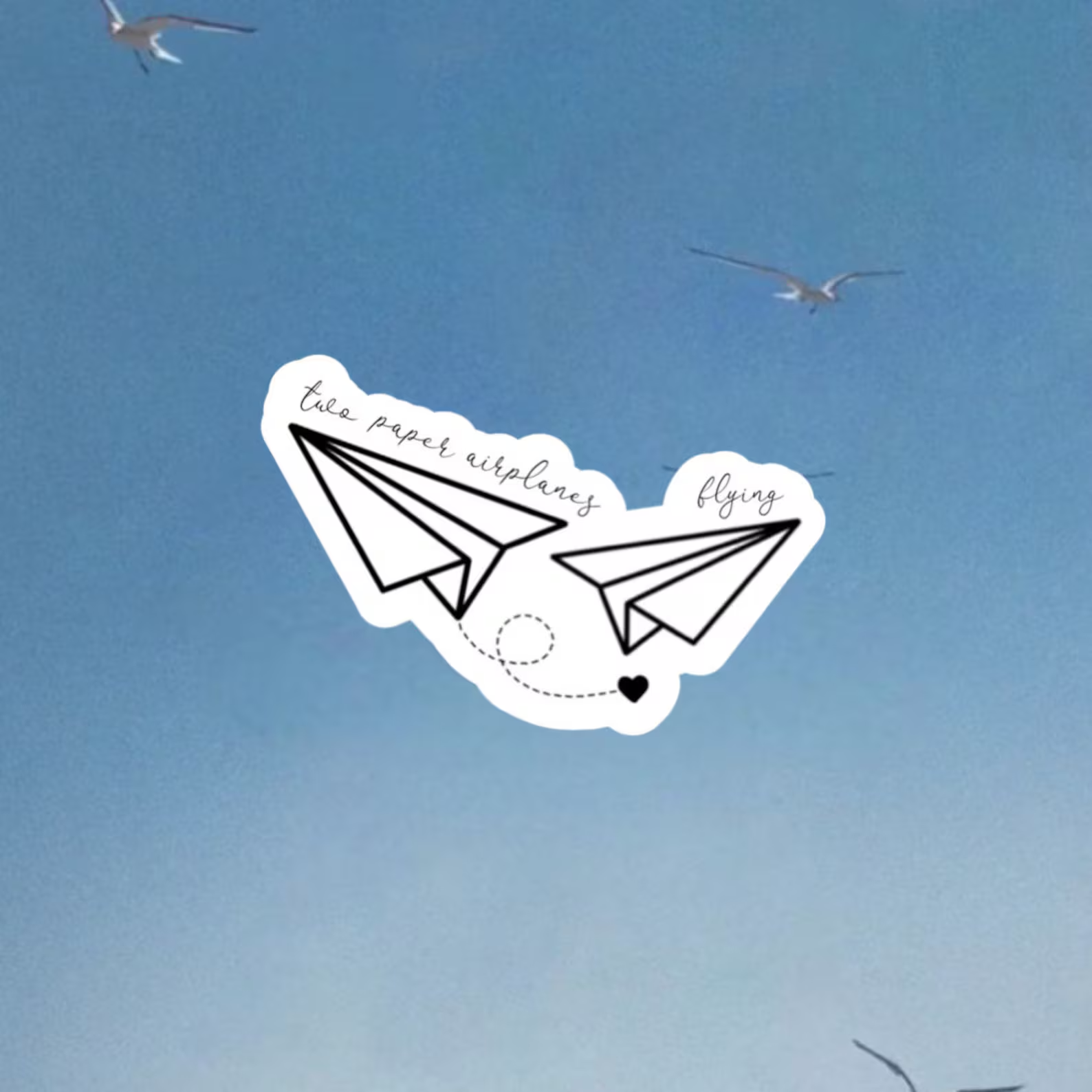 A sky view with seagulls flying and a sticker of two paper airplanes labeled 'the paper airplane' and 'flying,' connected by a dashed line and a small black heart.
