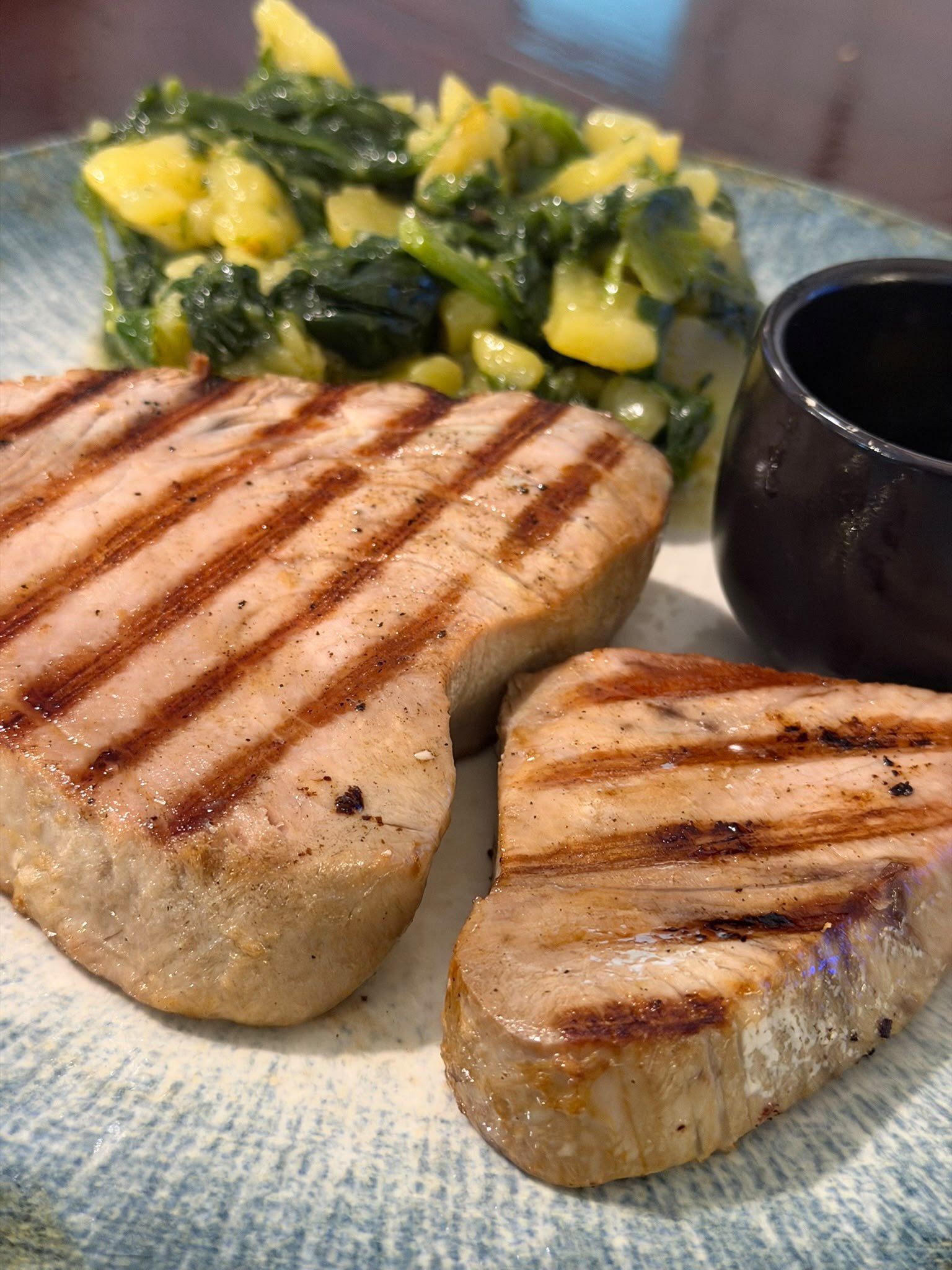 Close-up of grilled chicken breast and a side salad with chopped cucumbers and leafy greens on a blue plate, with a glass of dark soda.