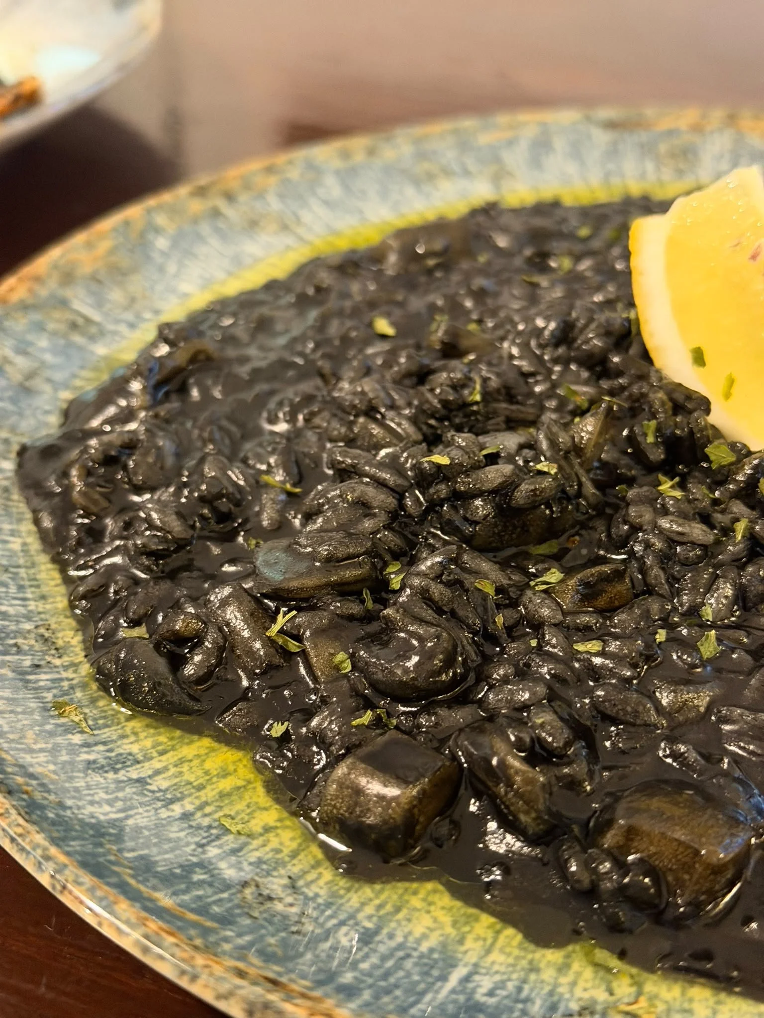 Close-up of black rice with lemon wedge on a colorful ceramic plate.