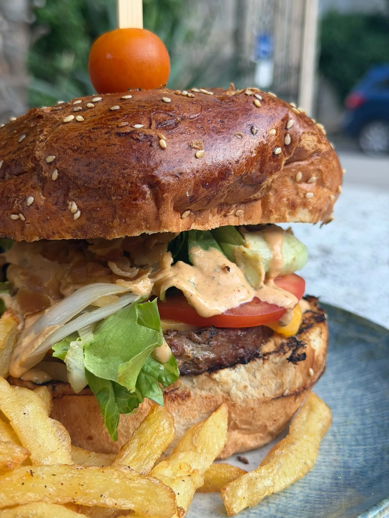 Close-up of a gourmet burger topped with lettuce, tomato, cheese, grilled patty, and a sesame seed bun, served with French fries.