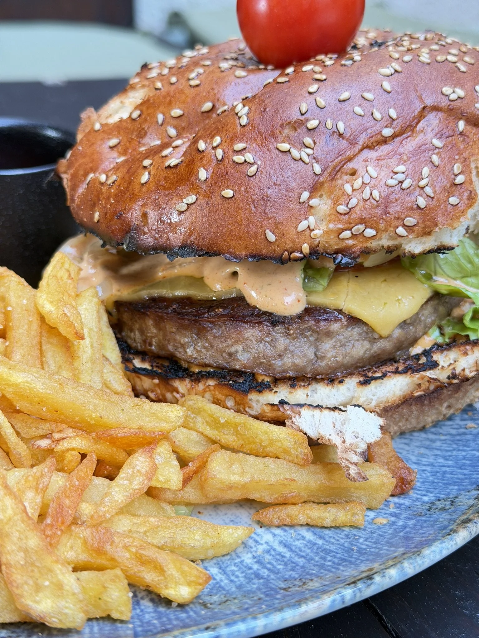 A cheeseburger with a sesame seed bun, lettuce, cheese, and a beef patty, served with a side of French fries on a blue plate.