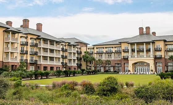 An apartment complex with multiple stories, balconies, and a central entrance, surrounded by a well-maintained lawn and greenery.