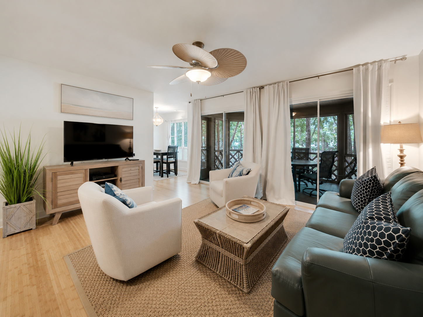 Living room with a sofa, armchair, coffee table, TV, and sliding glass door leading to a screened balcony with outdoor seating.