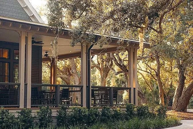 A house with a porch, surrounded by trees and bushes, with sunlight filtering through the leaves.