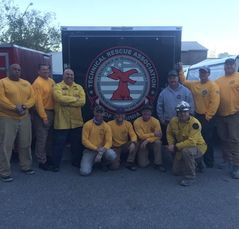 Group of people in rescue uniforms and gear posing in front of a rescue association truck with a logo for the Technical Rescue Association of Virginia.
