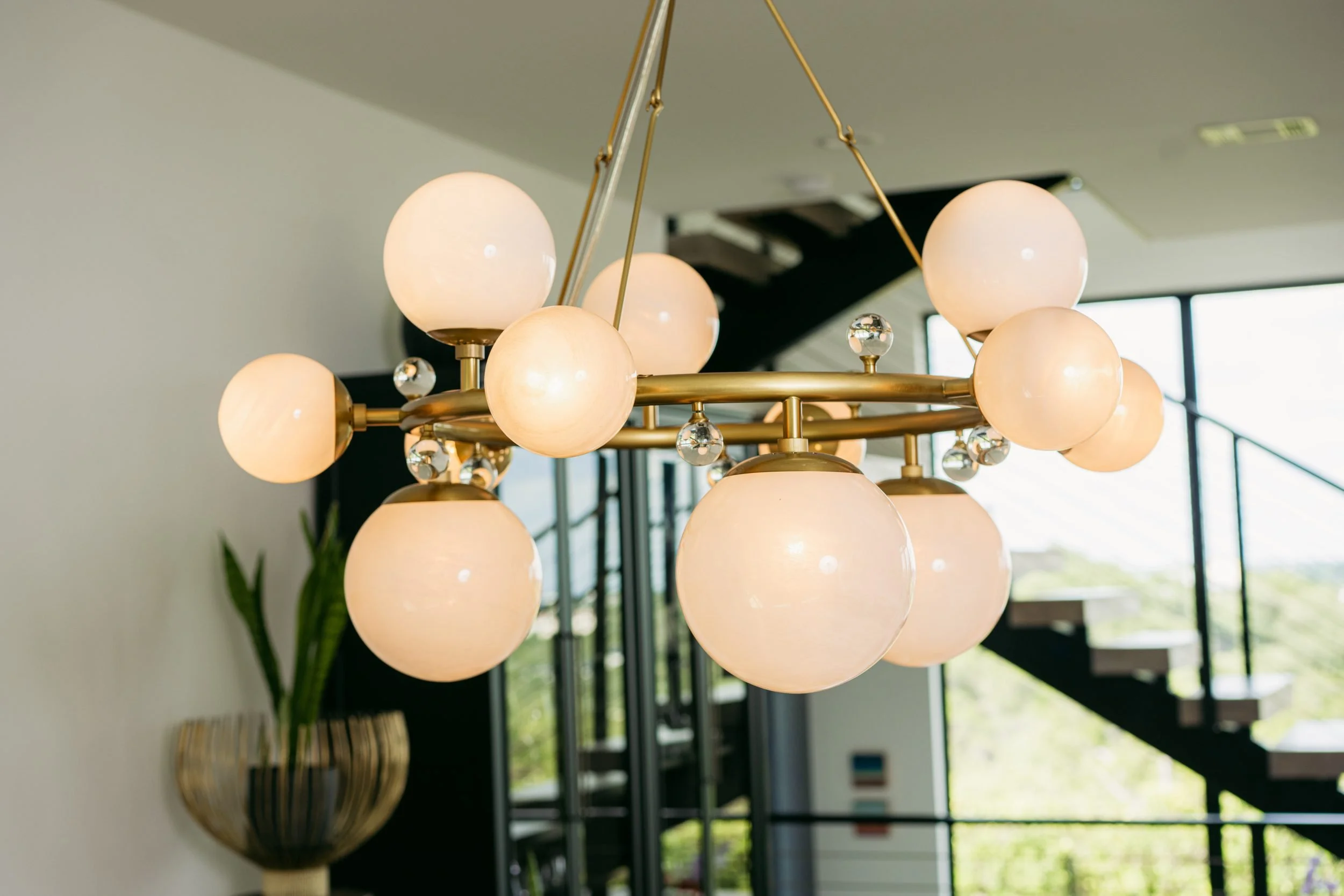 A brass globe chandelier set against the floating staircase and the treetops.