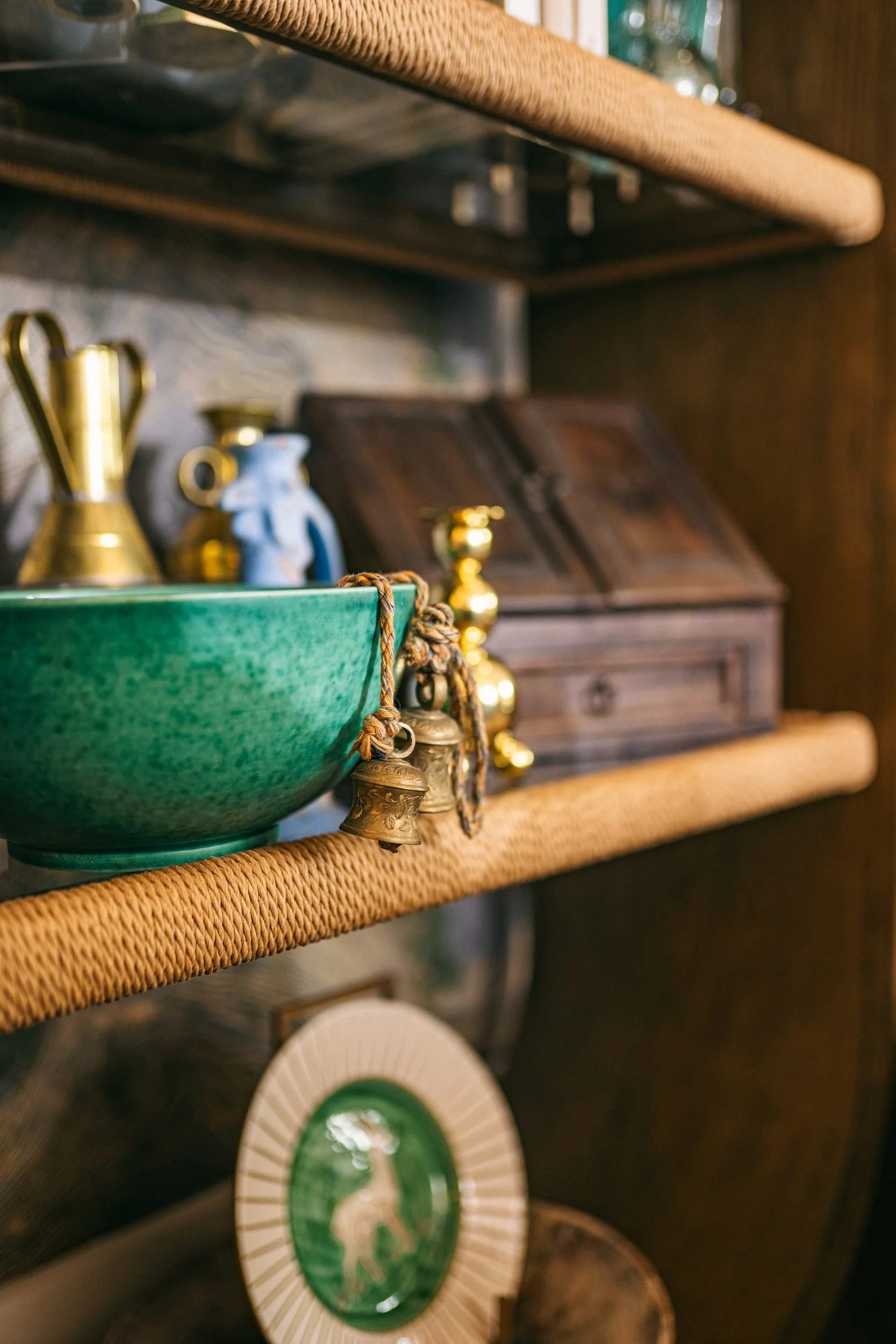 A green-glazed bowl and brass vessels on a cane-edged shelf — Texture, in the Sensory Living Method™.