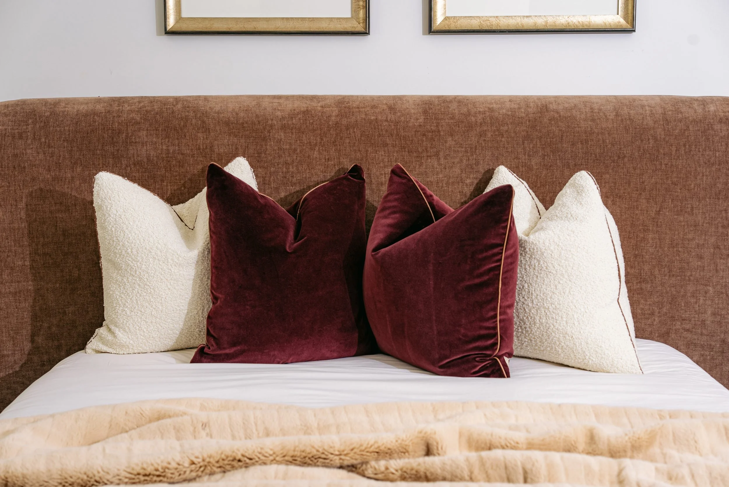 A bed layered with oxblood velvet and ivory pillows against a mohair headboard.