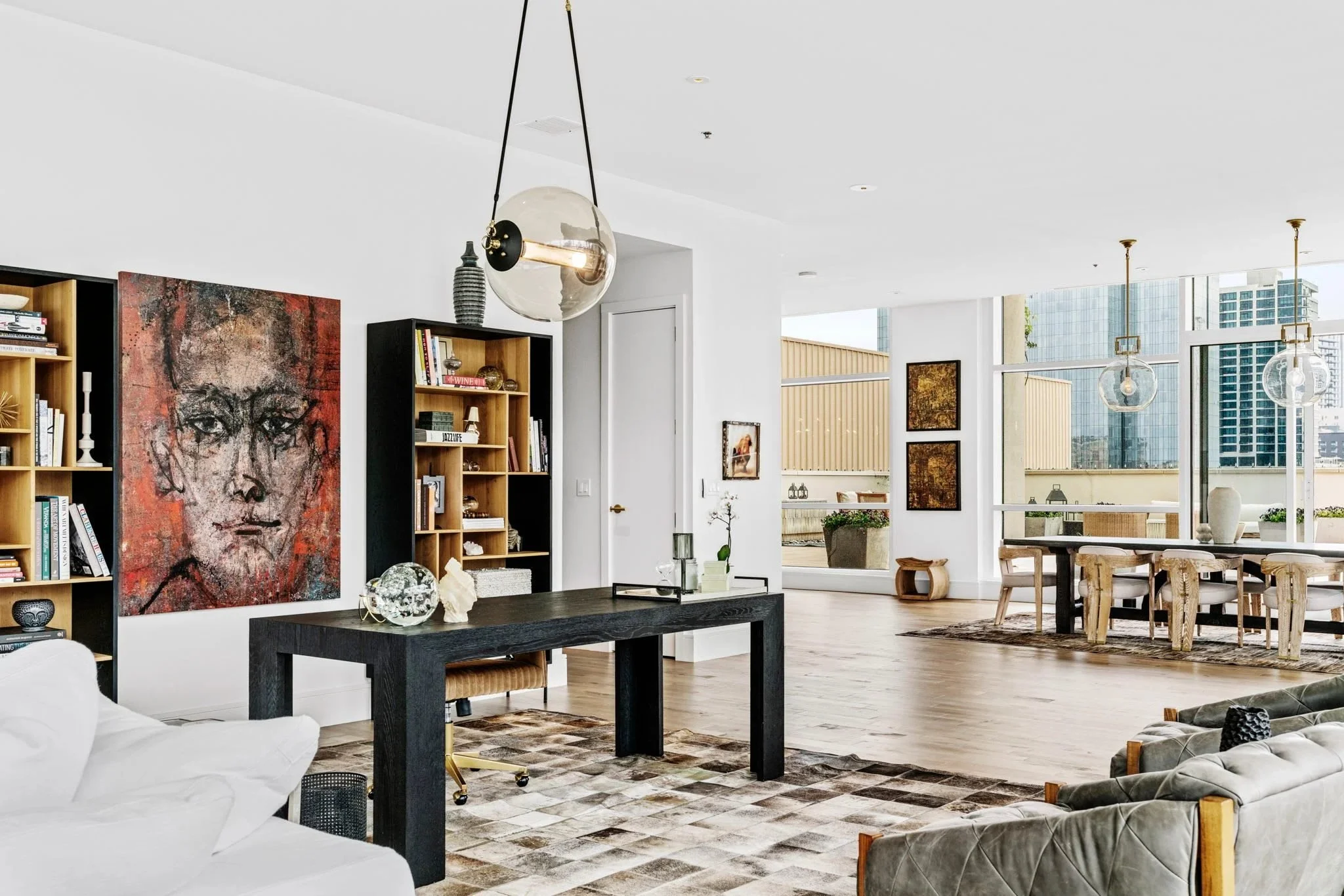 The great room, with a large-scale portrait and a black writing desk against the city windows.
