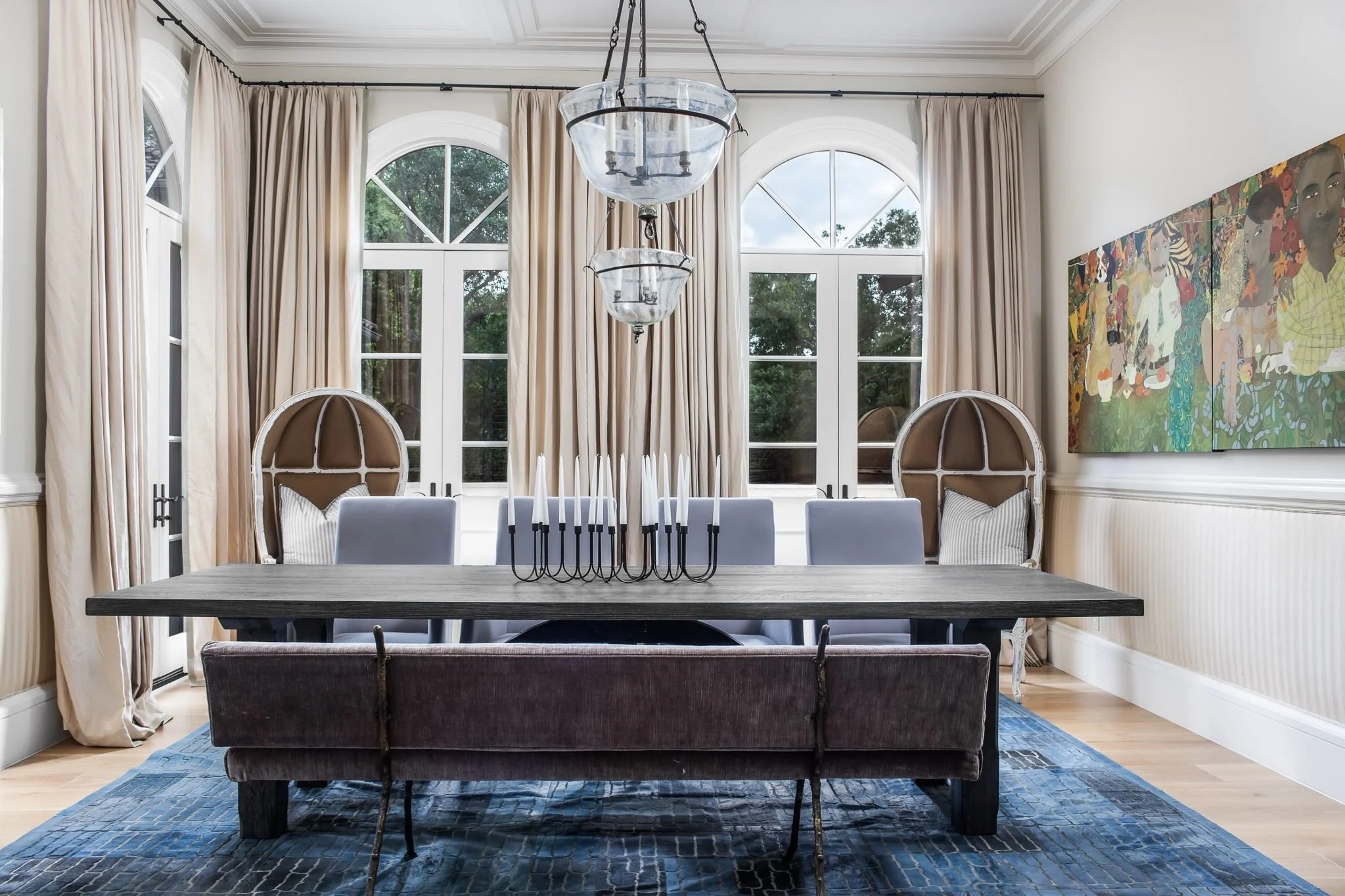 A dining room with arched windows, a long table and an oversized painting.