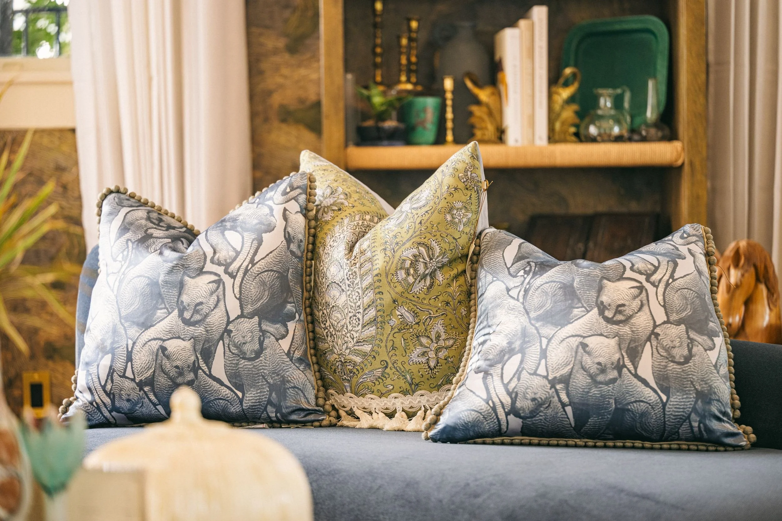 Three embroidered and fringed pillows layered on a blue velvet sofa.
