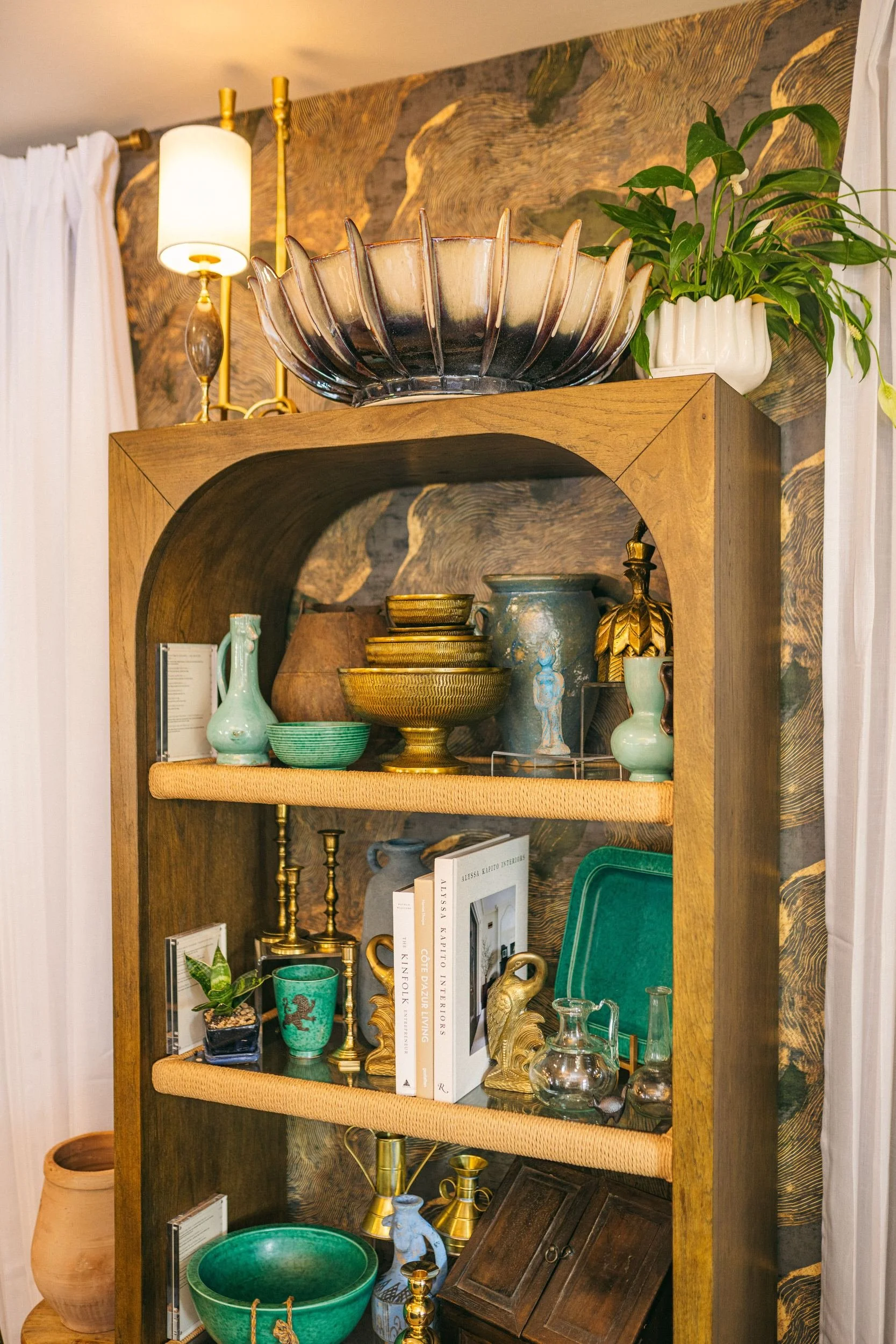 An arched oak shelf of glazed vessels, brass and books.
