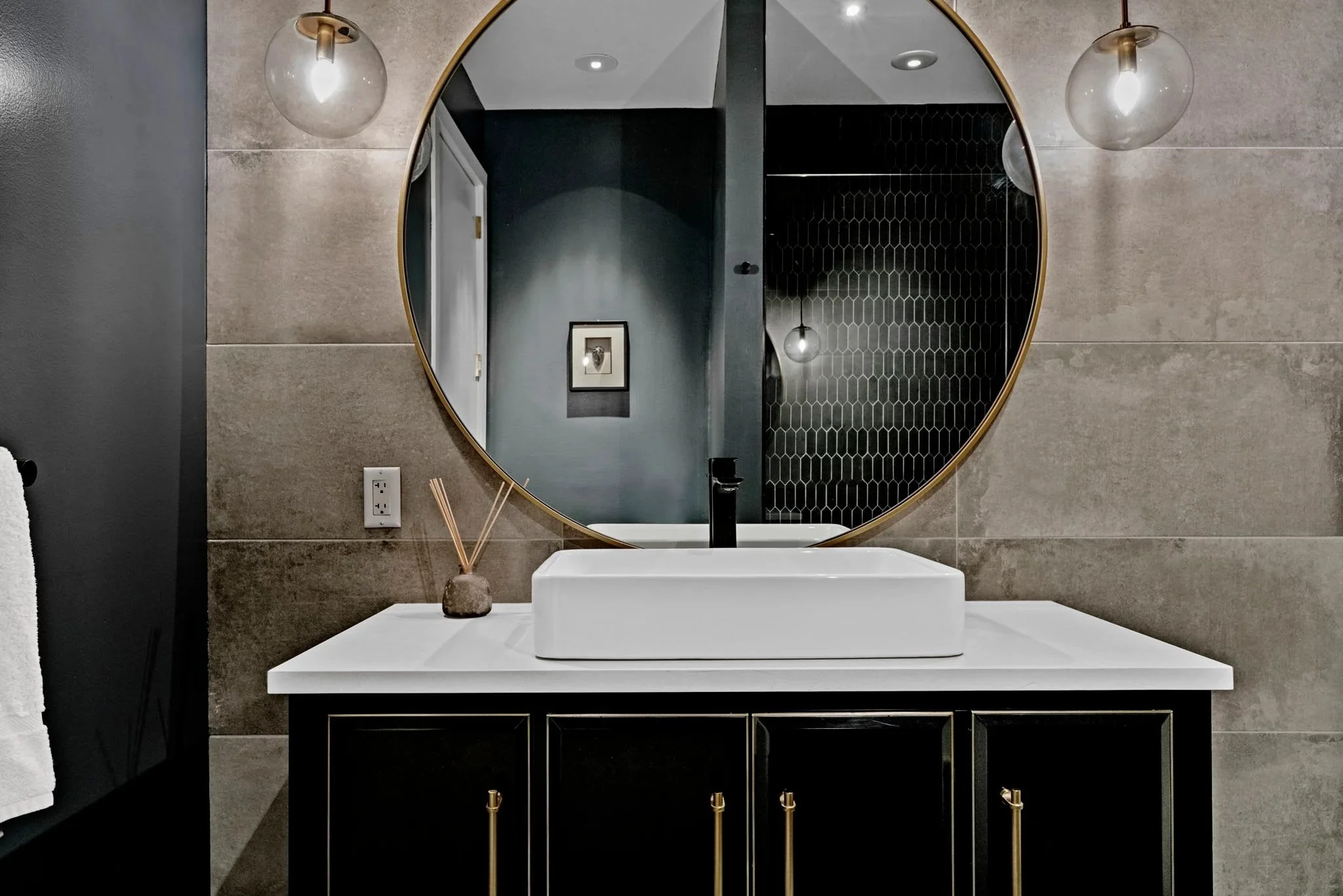 A bath in concrete tile and black, with a round brass mirror and glass pendants.
