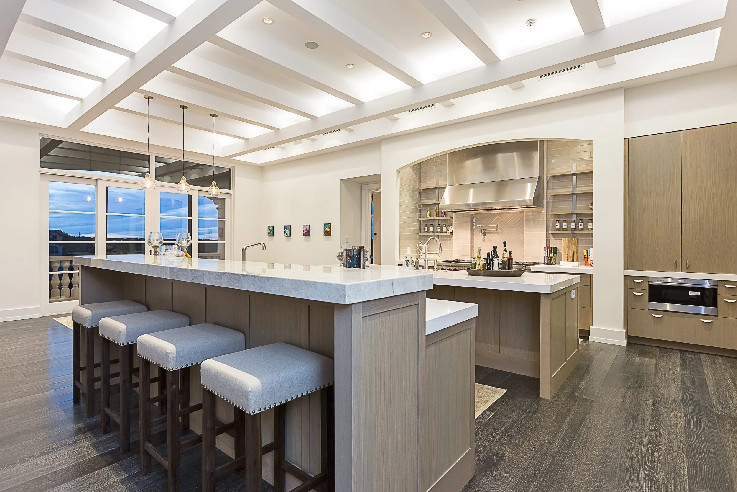 A white kitchen with a long island under a coffered ceiling.