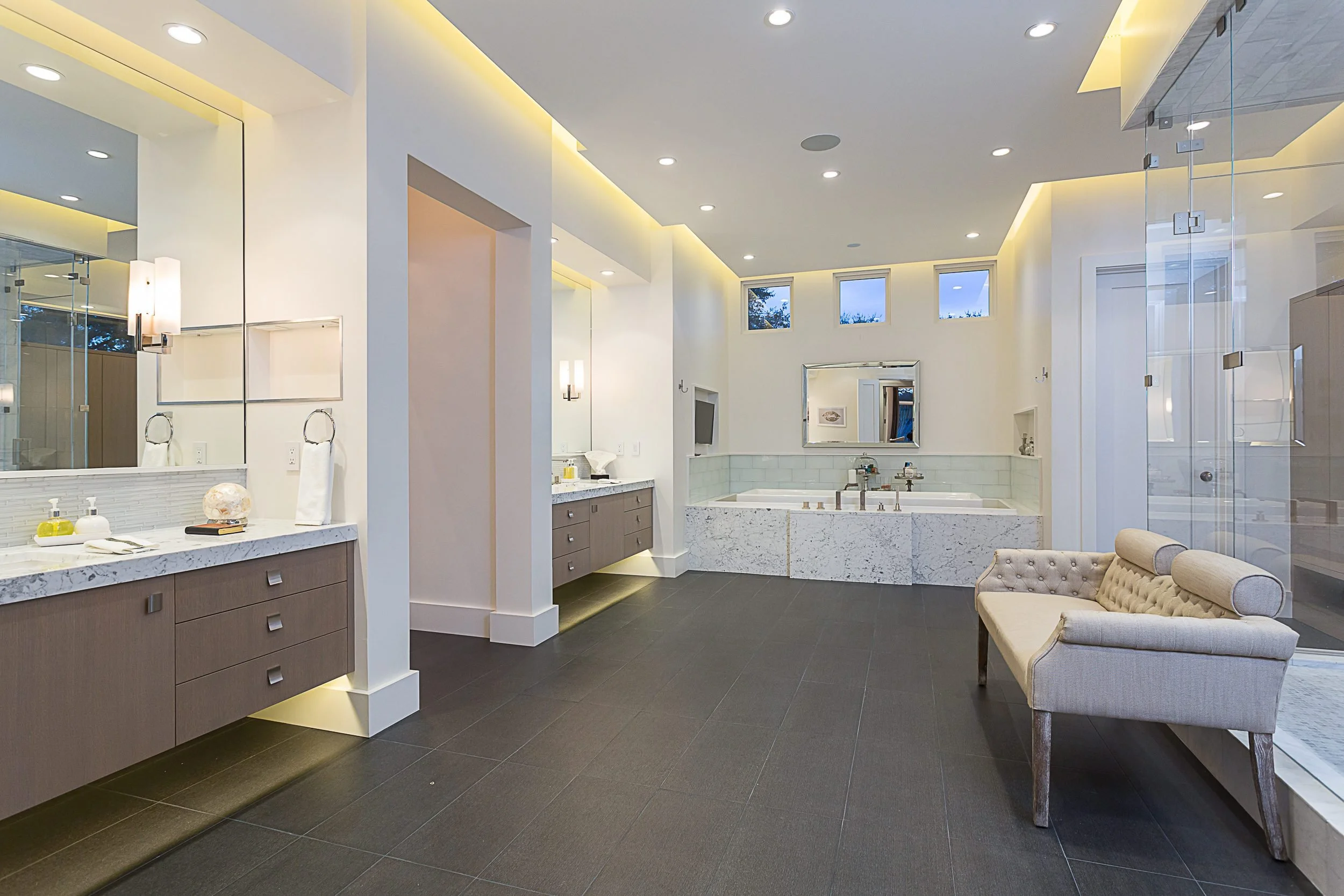 A primary bath with a freestanding tub, soft cove lighting and an upholstered bench.