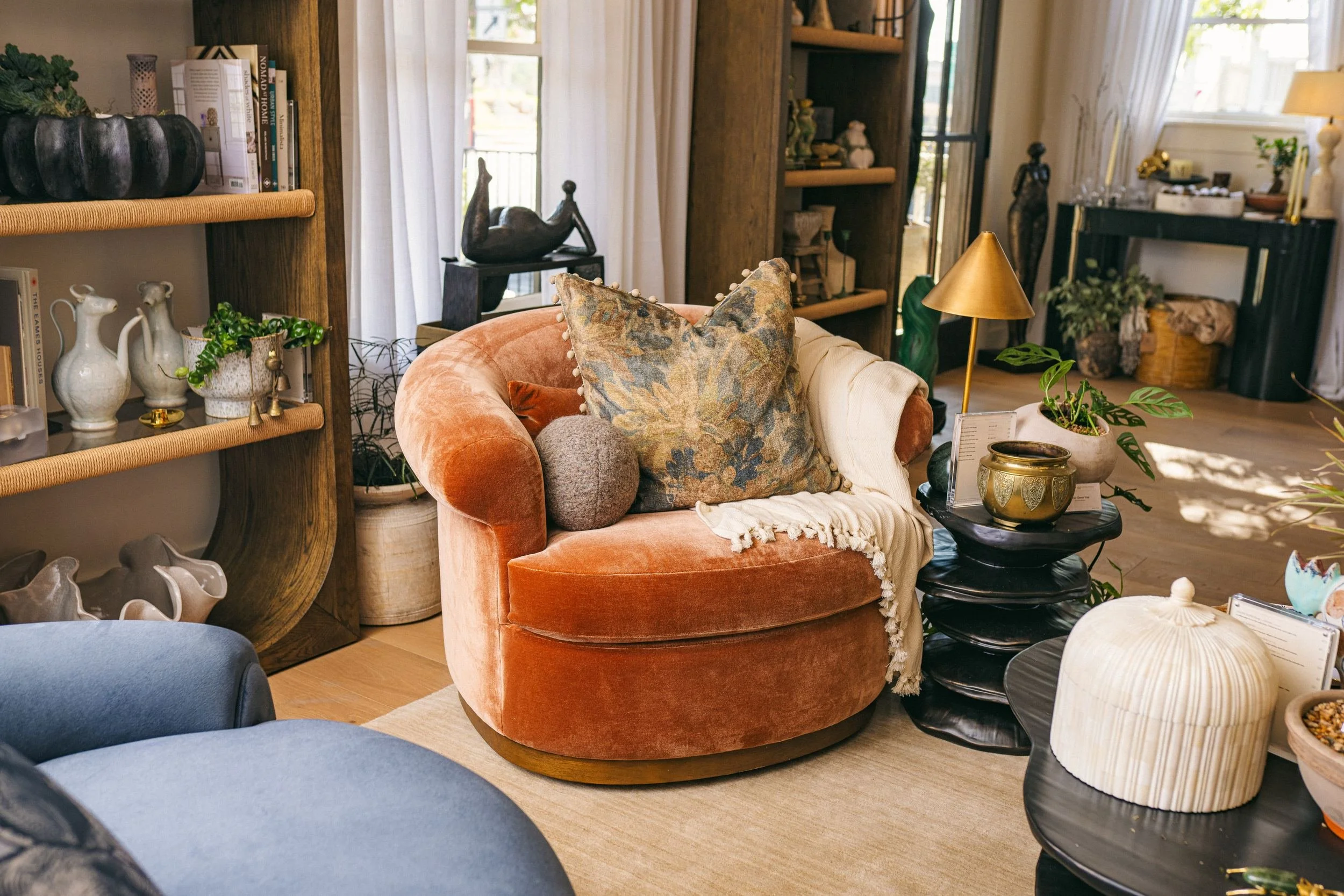 A rust velvet swivel chair with an embroidered pillow beside the studio shelves.