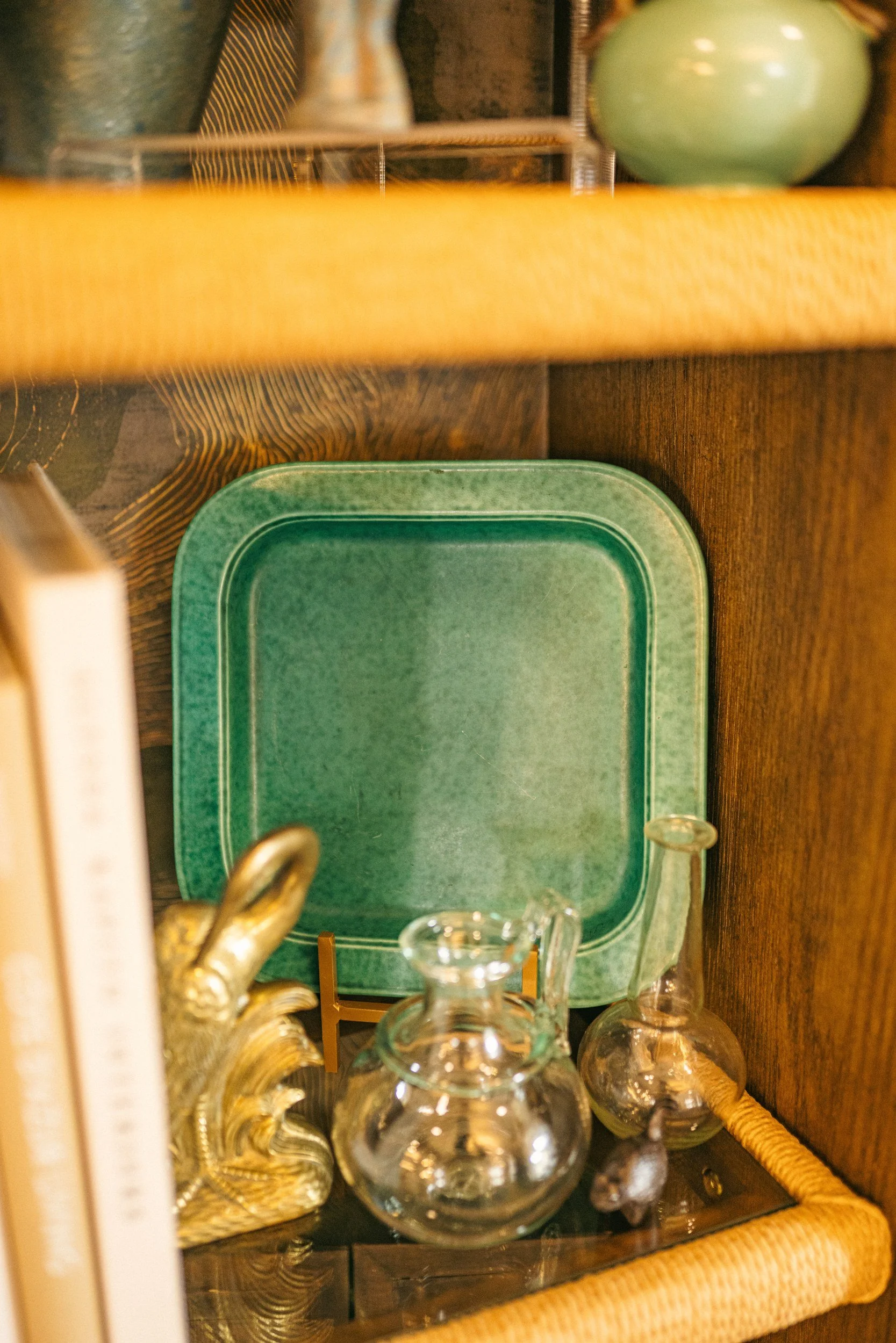 A wooden cabinet with a green tray or platter inside, surrounded by glassware and decorative items.