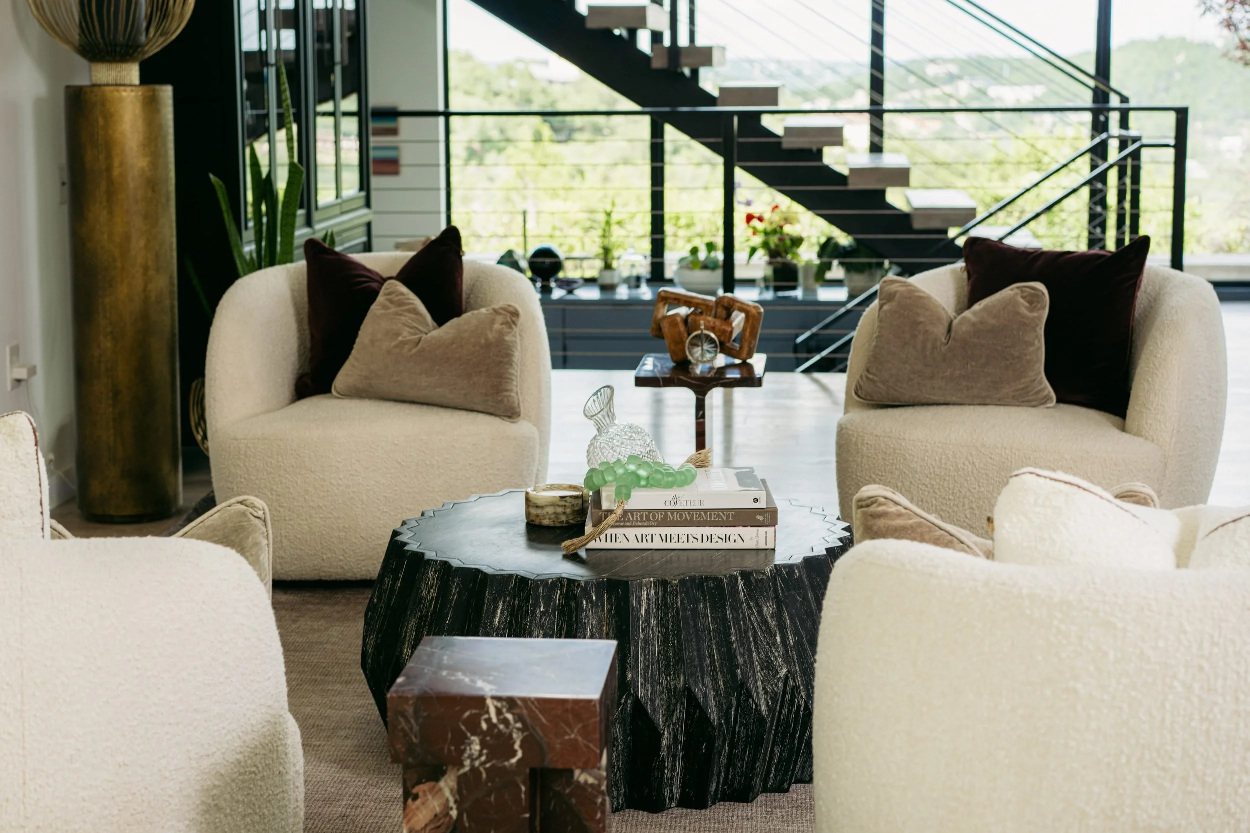 Bouclé chairs with velvet pillows beneath the steel staircase, the hills beyond the glass.