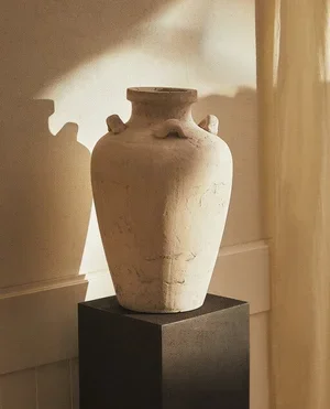 Ancient clay vase on a black pedestal in a museum setting.