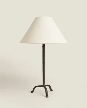 A floor lamp with a white lampshade and a black metal stand against a plain wall.