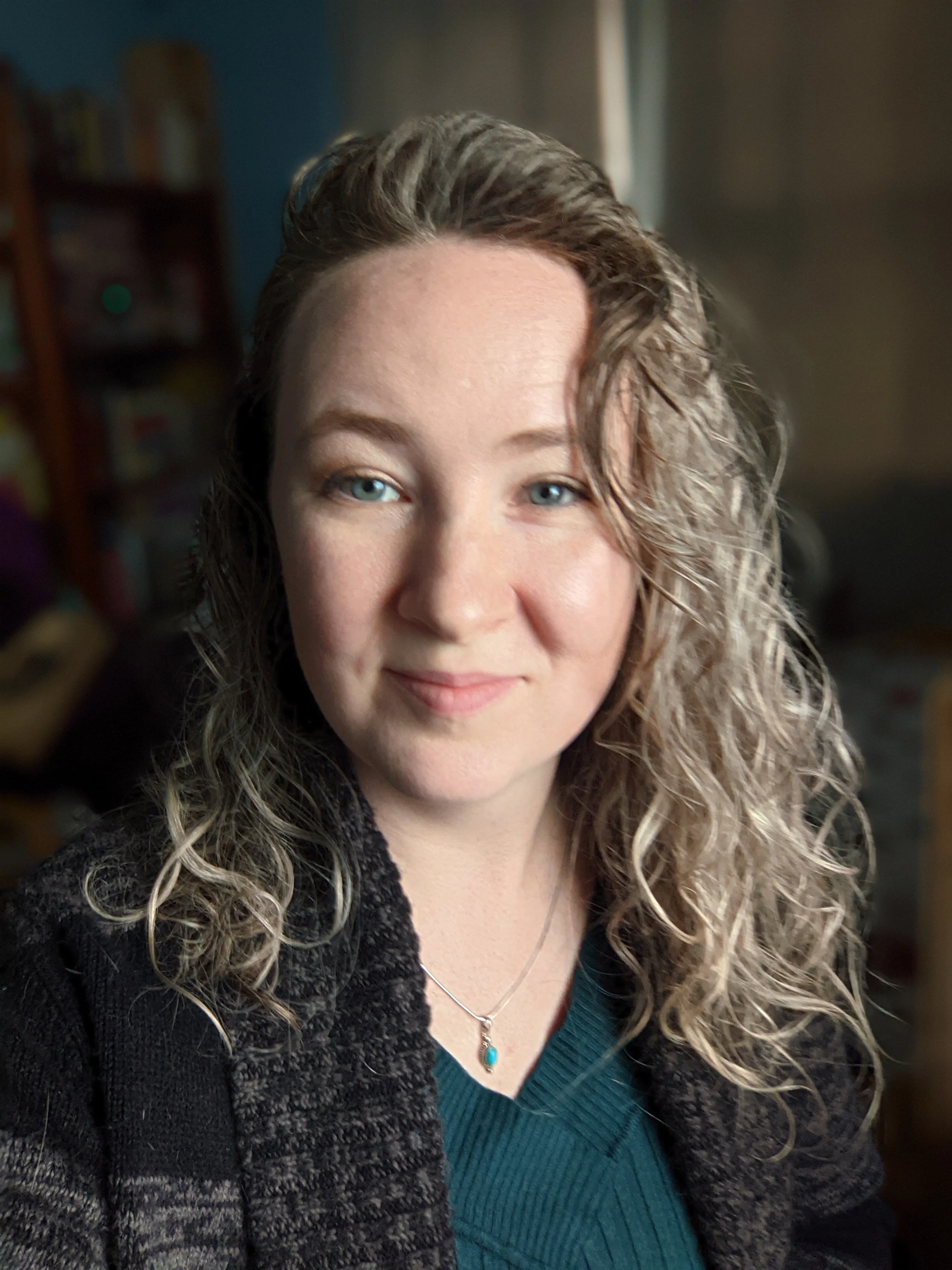 A photo of a woman, looking directly at the camera with a relaxed smile. The background is blurred.