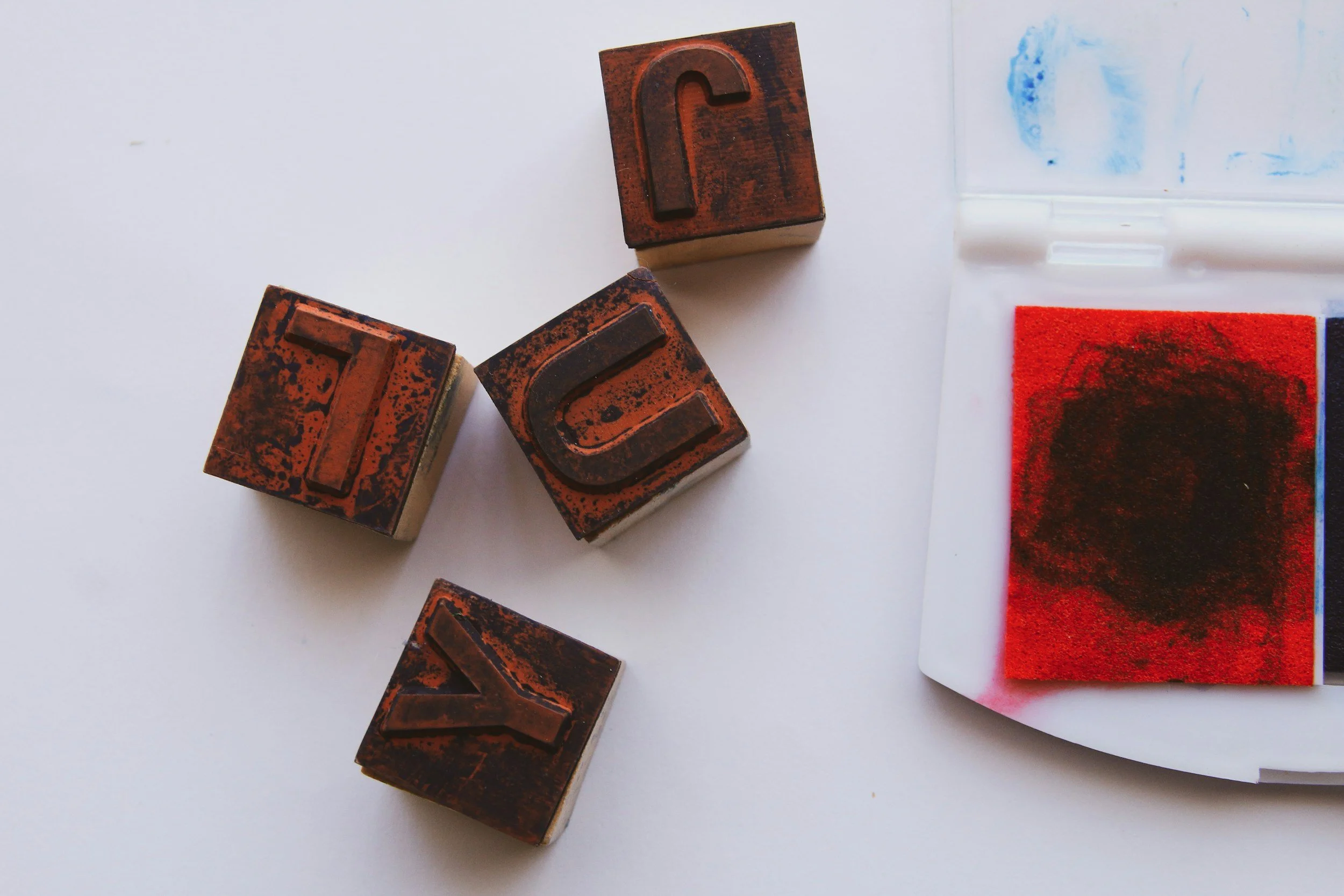 Rubber stamps with dark ink residue, placed on a white surface next to a piece of paper with red and black ink marks.