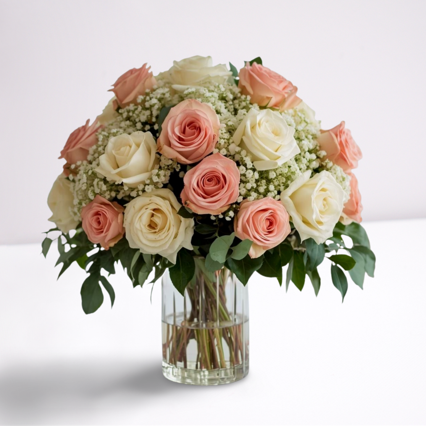 Large_floral_display_in_a_clear_vase_with_8_10_roses_in_it__Sitting_on_a_white_table_with_a_lot_of_light_surrounding_it_.png