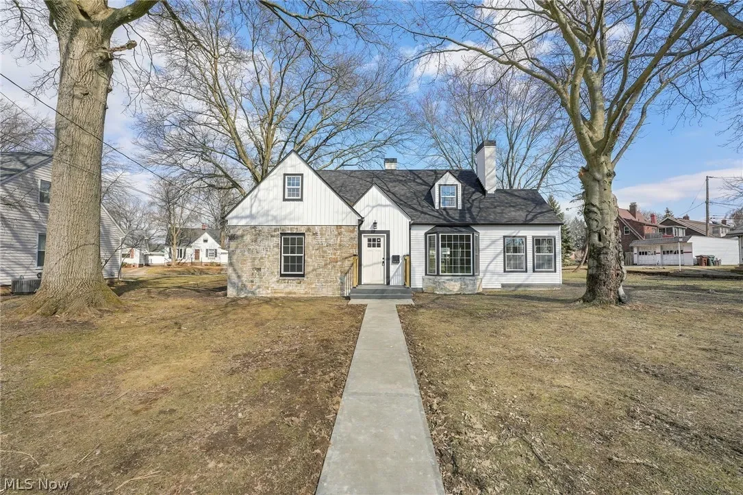 Complete home renovation in Parma, Ohio: front exterior with white siding, stone accents, updated windows and a concrete walkway to the entry.