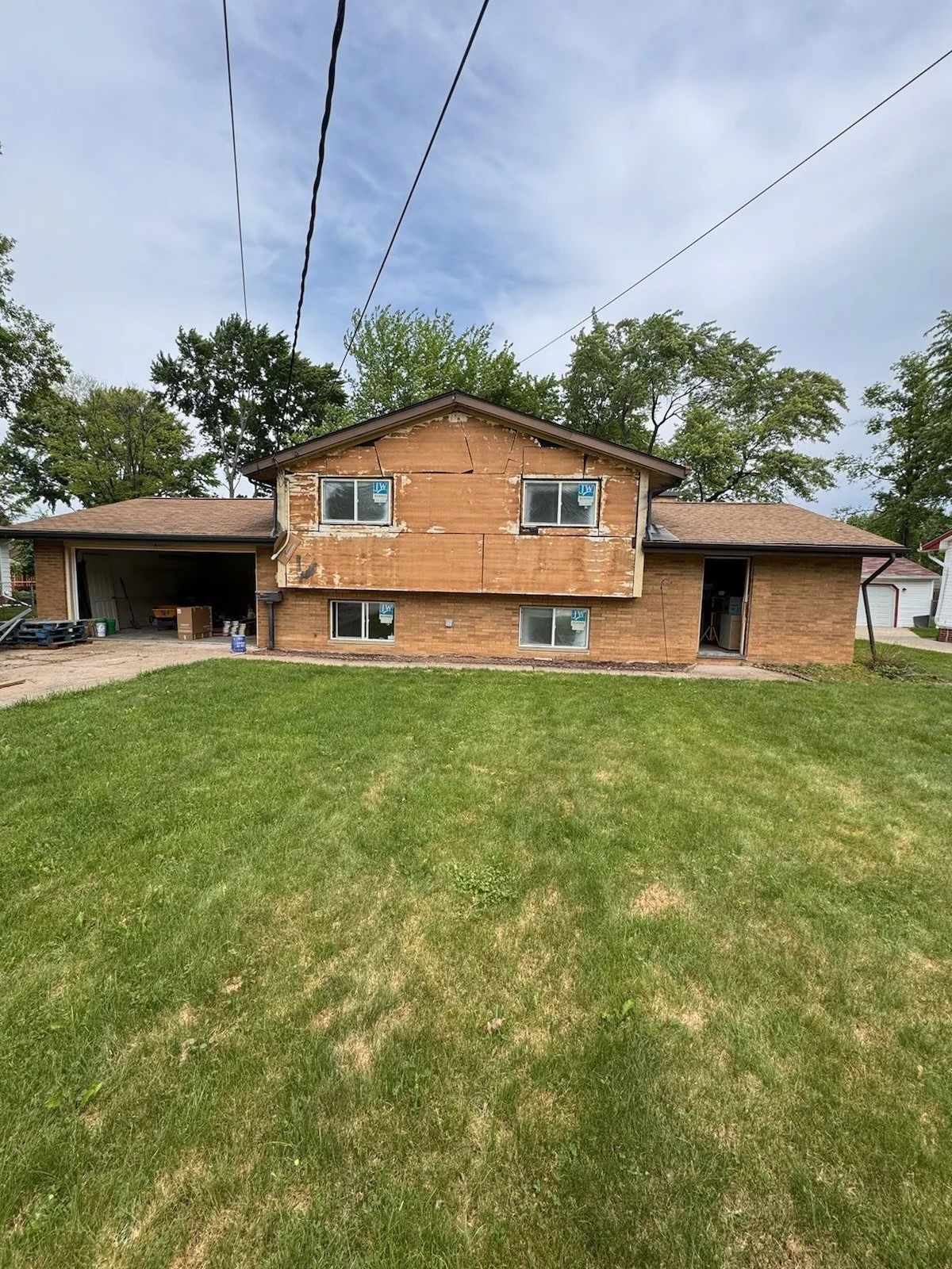 Split-level exterior, before: original orange-brown facade with brick and older siding, seen from the front lawn.