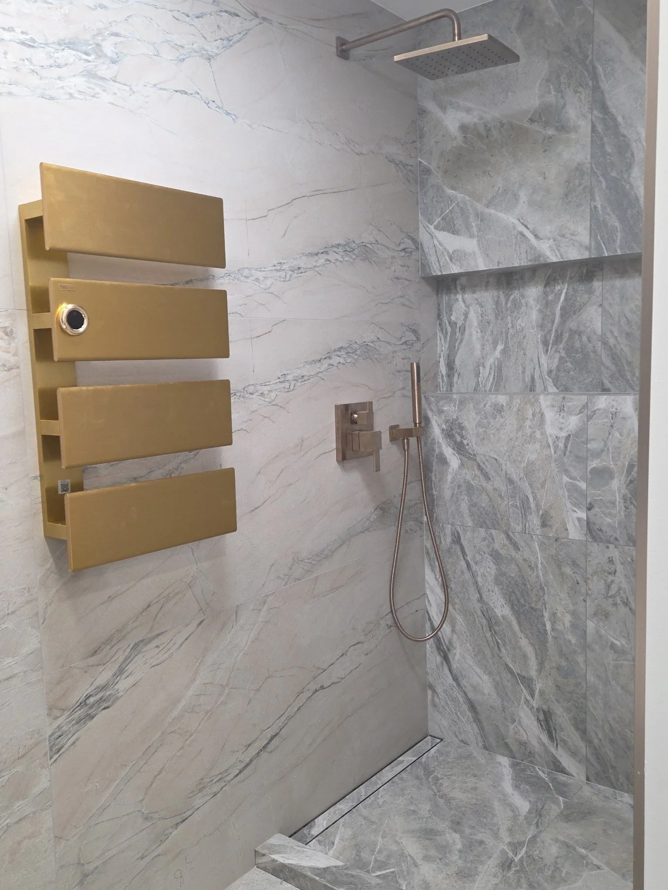 Bathroom detail: marble-look tile paired with gold heated towel racks. Gold finishes are replacing black.