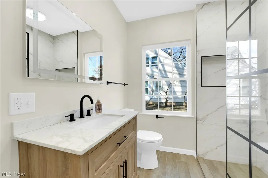 Bathroom: wood-tone vanity with a white countertop, black faucet and hardware, and a window bringing in natural light.