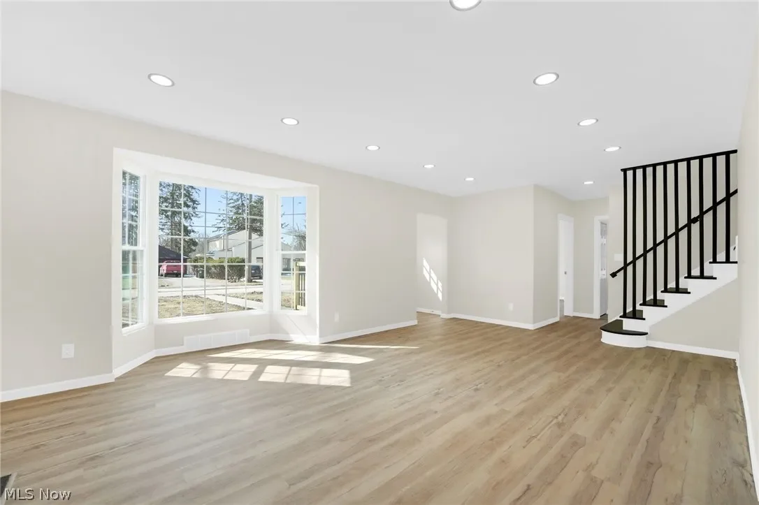 Living area: bright open room with plank flooring, recessed lighting, a large bay window and a staircase with modern black balusters.
