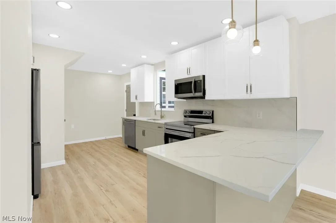 Kitchen: another view of the two-tone kitchen with stainless appliances, an L-shaped counter and pendant lighting.