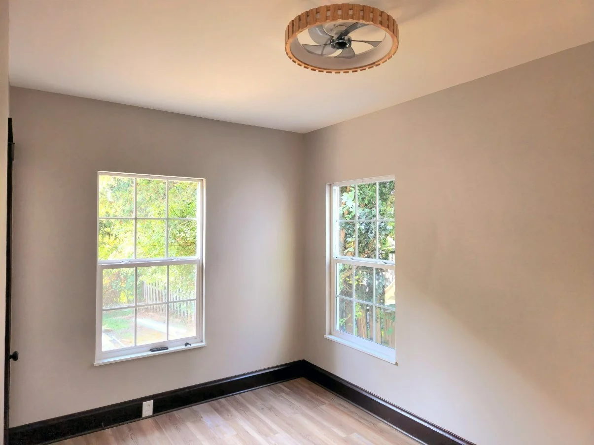 Completed corner room with two windows, dark trim and warm flooring