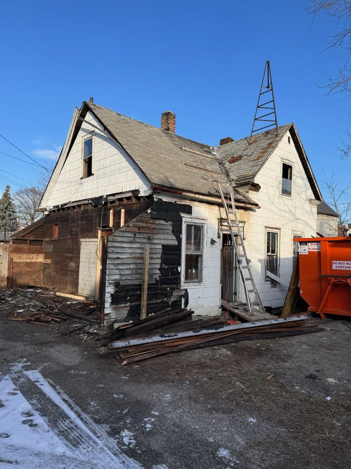 Before: the original gabled home stripped down during demolition, with old siding and framing exposed and a dumpster on site.