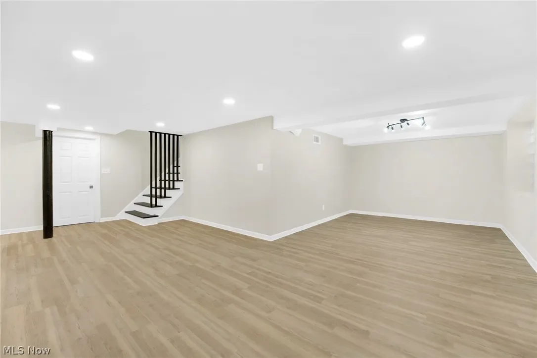 Finished basement: open, bright space with plank flooring, recessed lighting and a black-baluster staircase at left.