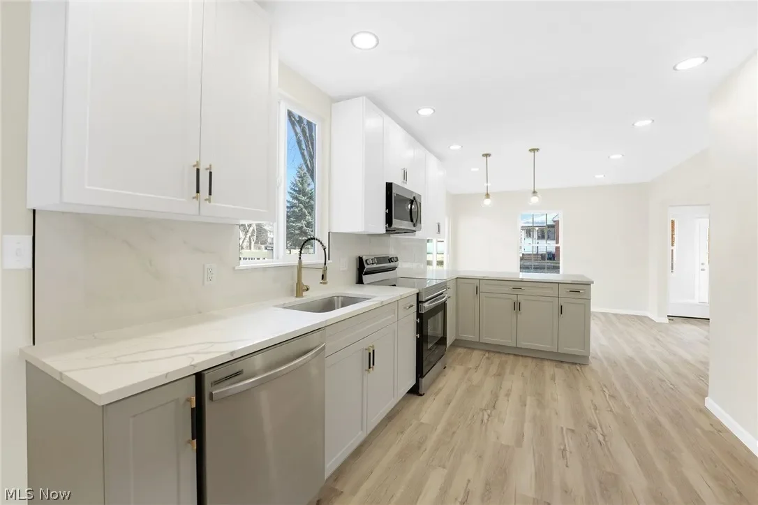 Kitchen: two-tone cabinetry with white uppers and gray lowers, light countertops, stainless appliances, pendant lighting and wood-look flooring.