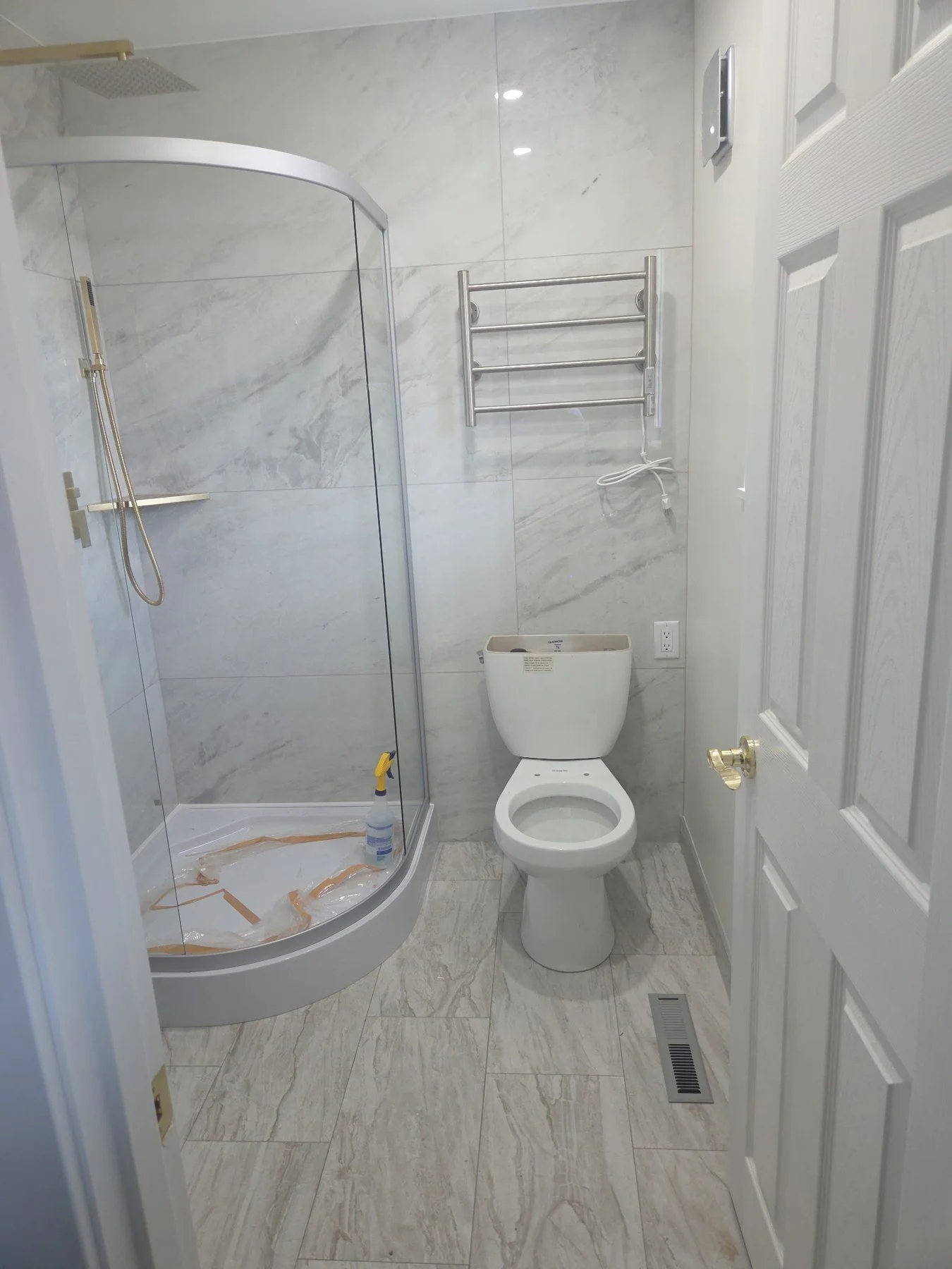 Compact bathroom: corner shower with a curved glass enclosure, marble-look tile and a wall-mounted towel rack.