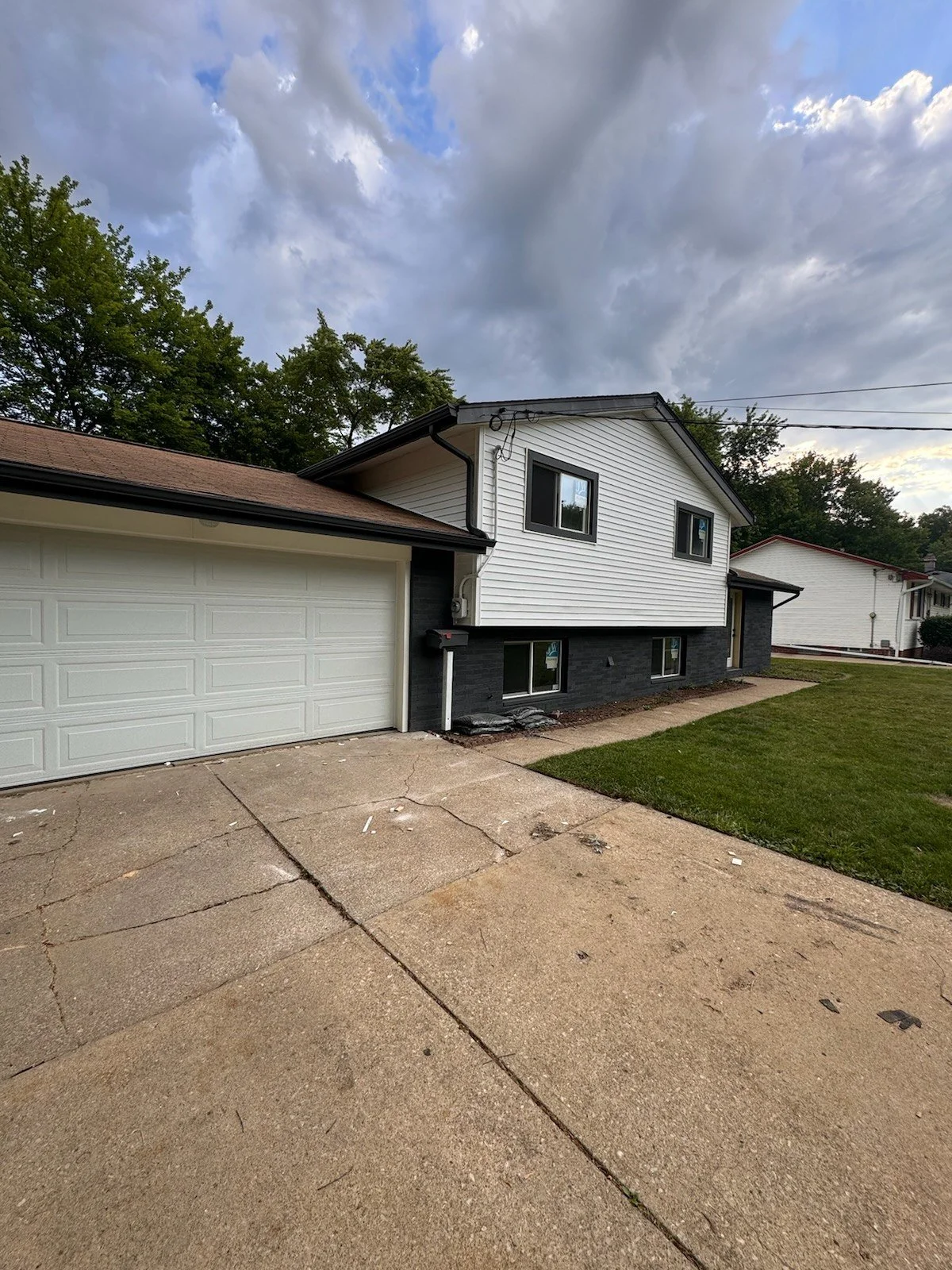 Split-level exterior, after: driveway-side view showing light siding, dark lower walls and the attached garage.